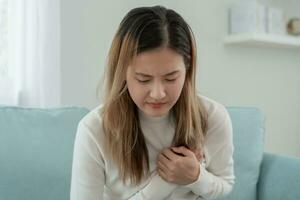 mano hold il petto con cuore attacco sintomi, asiatico donna Lavorando difficile avere il petto dolore causato di cuore patologia, perdere, dilatazione, allargata coronario cuore, stampa su il il petto con doloroso espressione foto