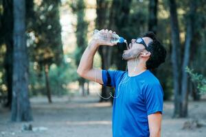 bianca uomo potabile acqua e ascoltando per musica nel un' parco mentre esercizio. foto