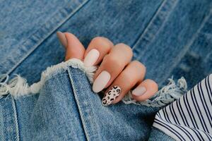 bellissimo femmina mani con manicure su il sfondo di denim. elegante chiodo design. autunno manicure con beige colore e leopardo modello su il chiodo. foto