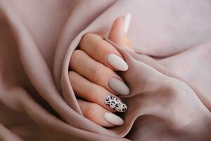 un' donna di mano con un' bellissimo manicure è Tenere un' seta tessuto. autunno tendenza, beige colore lucidatura con leopardo modello su Chiodi con gel polacco, Gommalacca. copia spazio. foto