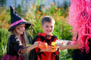 bambini trucco o trattare nel Halloween costume . un' poco ragazzi e un' ragazza nel tute ricevere caramella a partire dal un' donna vestito nel un' rosa parrucca . foto