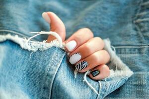 bellissimo femmina mani con manicure su il sfondo di denim. elegante chiodo design. manicure con nero e bianca zebra strisce su il chiodo. foto