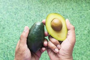 mano che tiene una fetta di avocado su sfondo verde foto