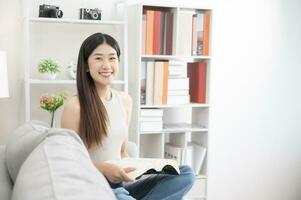 asiatico donna contento Sorridi bellissimo asiatico donna rilassante lettura libro nel Camera da letto a casa. casa rilassamento concetto foto