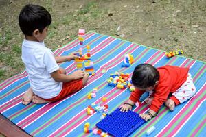 Due contento ragazzi nel società parco, contento asiatico fratelli chi siamo sorridente felicemente insieme. fratelli giocare all'aperto nel estate, migliore gli amici. bambino piccolo bambino ragazzo giocando con il suo contento fratello nel il giardino foto