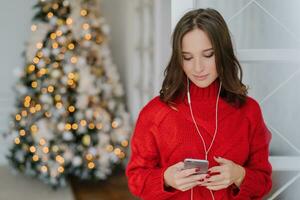 focalizzata donna legge notizia su Telefono con auricolari, di interno abete albero, alta velocità Internet. foto