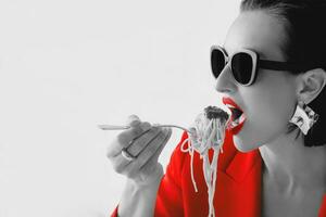 nero e bianca ritratto di alla moda elegante bellissimo donna nel occhiali da sole, rosso giacca mangiare spaghetti pasta. cibo, moda concetto foto