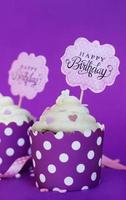 cupcakes alla vaniglia con piccoli cuori decorativi e segno di buon compleanno, su sfondo viola sfondo festa