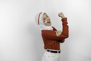 eccitato asiatico musulmano donna indossare un' rosso superiore e bianca hijab mostrando forte gesto di sollevamento sua braccia e muscoli sorridente con orgoglio. dell'Indonesia indipendenza giorno concetto. foto