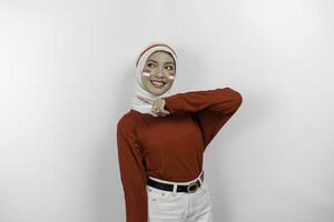 un' contento asiatico musulmano donna indossare rosso superiore e bianca hijab, e puntamento copia spazio accanto suo, isolato di bianca sfondo. dell'Indonesia indipendenza giorno foto