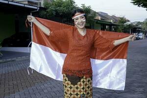 contento sorridente indonesiano donna indossare rosso kebaya Tenere dell'Indonesia bandiera per celebrare Indonesia indipendenza giorno. all'aperto servizio fotografico concetto foto