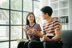 Due asiatico studenti apprendimento insieme in linea con un' computer portatile, tavoletta e precettore insieme nel vivente camera a casa. foto