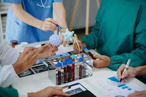 medico squadra avendo un' incontro con medici nel bianca laboratorio cappotti e chirurgico scrub seduto a un' tavolo discutere un' pazienti Lavorando in linea utilizzando computer nel il medico industria foto