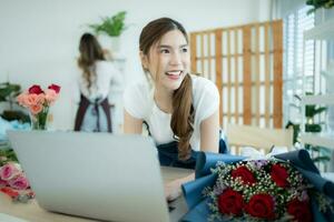 giovane asiatico donna fioraio Lavorando con il computer portatile nel fiore negozio foto
