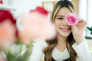 sorridente asiatico donna Tenere rosa fiore nel sua mano a casa foto