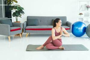 asiatico giovane salutare donna nel articoli sportivi praticante yoga a casa, sport ragazza Meditare nel vivente camera a casa foto