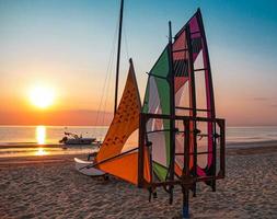 Multicolore vele windsurf e barca a motore sulla spiaggia vuota all'alba durante il bellissimo oceano sunrise a rivazzurra rimini italia costa adriatica foto