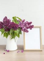 bouquet di fiori lilla in vaso e cornice di legno vuota foto