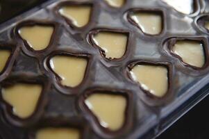 avvicinamento di cioccolato muffe nel il forma di cuori pieno di dolce cremoso Riempimento foto