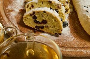 ritagliata Visualizza di tagliato fette di appena al forno tradizionale fatti in casa Tedesco Stollen pane cosparso con in polvere zucchero su di legno asse, tazza di salutare erbaceo bere. Natale cibo e bevanda sfondo foto