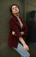 attraente alla moda giovane 30 anni vecchio europeo brunetta donna con elegante corto taglio di capelli nel casuale indossare pendente su il marmo parete di un' aziendale edificio foto