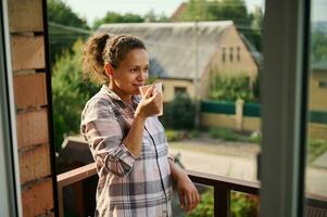 bella giovane ispanico donna rilassante su balcone Tenere un' tazza di caffè o tè. foto