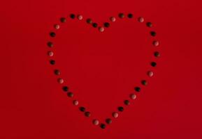 piatto posare composizione con cuore forma foderato con Multi colorato cioccolato pillole su rosso sfondo foto