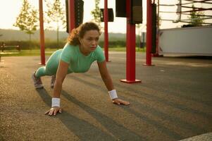 giovane misto gara, africano americano donna atleta Lavorando su all'aperto, fare sollevamento su campo sportivo nel estate. salutare attivo stile di vita e fitness concetto foto