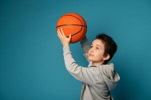 adolescenziale ragazzo, pallacanestro giocatore, in posa al di sopra di blu sfondo con un arancia palla nel il mani foto