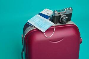 studio tiro di un' valigia, Vintage ▾ telecamera, passaporto con aria biglietto e imbarco passaggio, medico maschera isolato al di sopra di blu sfondo con copia anno Domini spazio. turismo e viaggio concetto foto