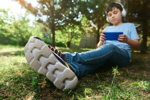 messa a fuoco per suola di il scarpe da ginnastica di adolescenziale ragazzo giocando virtuale in linea video gioco su smartphone. bambini e digitale dipendenza foto