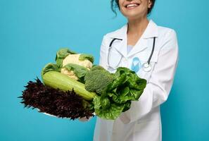 crudo la verdura, salutare vegano cibo, verdura e insalate nel il mani di sorridente dietologo indossare un' medico toga con blu diabete consapevolezza nastro, isolato al di sopra di colorato sfondo, copia spazio foto