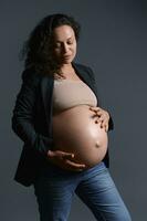 incinta donna colpi sua pancia al di sopra di un' grigio sfondo. 40 settimana. 9 mese di contento gravidanza. maternità. corpo positività foto