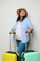 bellissimo incinta donna in viaggio all'estero, sorrisi guardare a parte, pose con valigie, isolato bianca studio sfondo foto