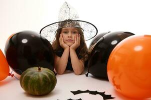 bella poco strega ragazza nel un' procedura guidata cappello dire bugie su un' bianca sfondo con copia spazio Il prossimo per fatto a mano provato pipistrelli, zucca e arancia nero palloncini. tradizionale evento, Halloween festa concetto. foto