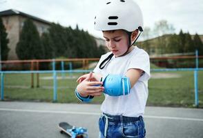 ritratto di un' bello ragazzo skateboarder indossare sicurezza casco mettendo su protettivo braccioli prima pattinando foto