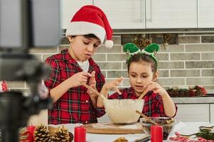 adorabile bambini nel rosso e verde scacchi Abiti, bellissimo poco ragazza indossare elfo cerchio e sua più vecchio fratello preadolescente ragazzo nel Santa cappello cucinando Natale biscotti insieme nel il casa cucina foto