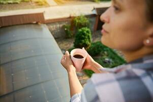 morbido messa a fuoco su il mani di donna Tenere tazza di caffè in piedi nel il balcone foto