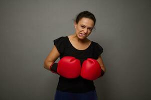 forte africano donna pose contro grigio parete sfondo con rosso boxe guanti. concetto di nero Venerdì e boxe giorno, soffio per prezzi con copia spazio per annuncio pubblicitario foto