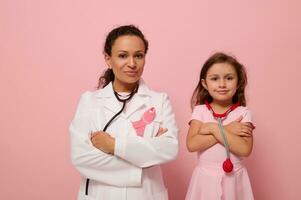 affascinante donna medico nel bianca medico toga sta Il prossimo per un' carino poco ragazza nel rosa, tutti e due con croci braccia su il petto e indossare un' rosa nastro, simbolo di Seno cancro consapevolezza giorno. medico concetto foto