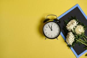 piatto posare di delicato bellissimo elegante mazzo di astri autunno fiori su un' vuoto vuoto lavagna con spazio per testo e un allarme orologio isolato su giallo sfondo foto