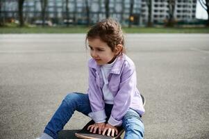 adorabile femmina bambino seduta su di legno skateboard contro sfocato edifici sfondo foto