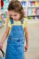 poco ragazzo, prescolastico ragazza vestito nel giallo maglietta e denim vestire, con shopping carrello, nel il scuola Stazionario memorizzare foto