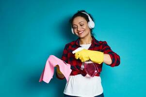giovane donna con un' bellissimo Sorridi l'applicazione un' detergente spray su un' straccio, pulizia concetto tiro su blu sfondo foto