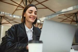 bellissimo donna attività commerciale persona, copywriter, sviluppatore, libero professionista, giornalista Lavorando remoto su computer portatile, scrittura testo, godendo lontano opera nel al di fuori estate caffetteria su bellissimo presto primavera giorno foto