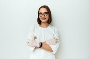 affascinante medico nel bianca medico laboratorio cappotto pose nel davanti di telecamera con attraversato braccia su il petto contro bianca sfondo con copia spazio foto