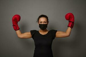 donna pugile nel nero medico protettivo maschera e boxe guanti solleva mani nel vincitore posizione. tiro per boxe giorno e nero venerdì. concetto di soffio per prezzi su grigio sfondo con copia spazio foto