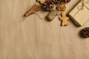 piatto posare di fatto a mano Natale composizione con un' regalo nel mestiere involucro carta, Pan di zenzero biscotti , legato cannella nel un' corda e pino coni su un' Marrone cartone sfondo con copia anno Domini spazio foto