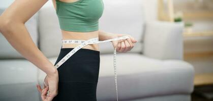 asiatico salutare donna dieta peso perdita. sottile donna misurazione vita con misurare nastro dopo dieta a casa peso controllo. foto