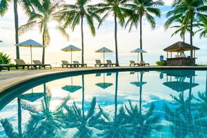 bellissimo ombrellone di lusso e sedia intorno alla piscina all'aperto in hotel e resort con palme da cocco al tramonto o all'alba sky foto